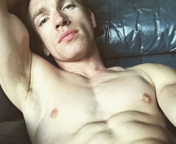 A photo of Sean Cody's porn star, Nick Gruber. He is shirtless laying on a black, leather couch. 