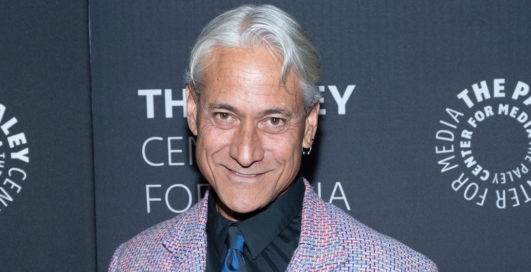Greg Louganis wearing a black dress shirt, black and blue striped tie and colorful sport coat.