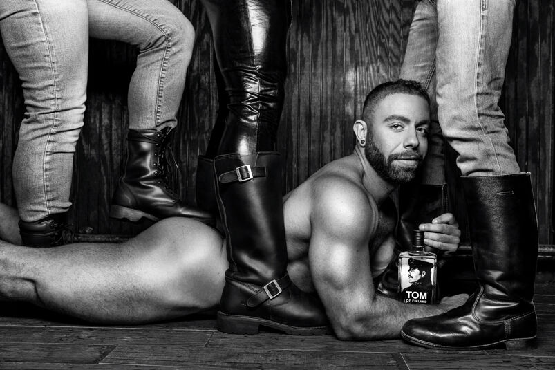 A nude muscular man is lying on the floor with a bottle of vodka, surrounded by standing men wearing leather boots. 