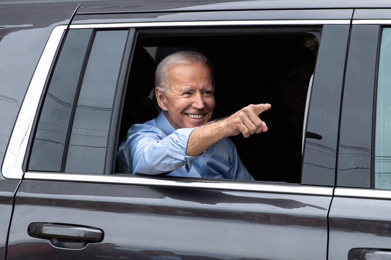 Joe Biden, wearing a blue dress shirt, sticking his finger out of a car window.