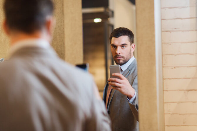 young man in suit with smartphone taking mirror selfie at clothing store