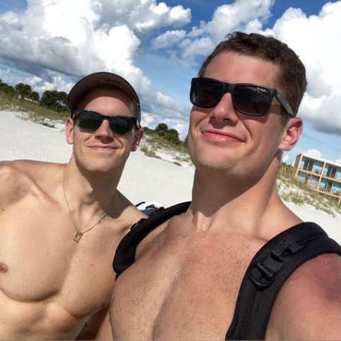 To buff men shirtless, stand side-by-side in sunglasses on the beach
