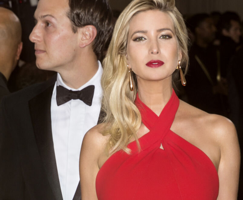 Ivanka Trump wearing a red dress with Jared Kushner, in a tuxedo, standing behind her.