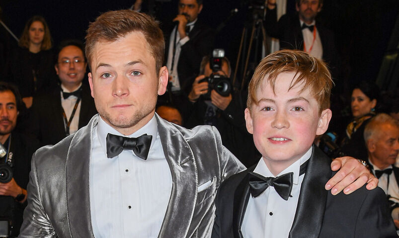 Taron Egerton and Kit Connor on a 2019 'Rocketman' red carpet. The pair are wearing suits and bowties.