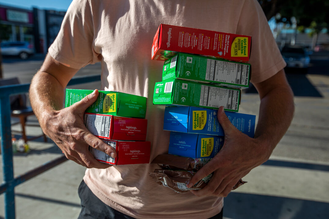 A man carries ten packages of Girl Scout cookies.