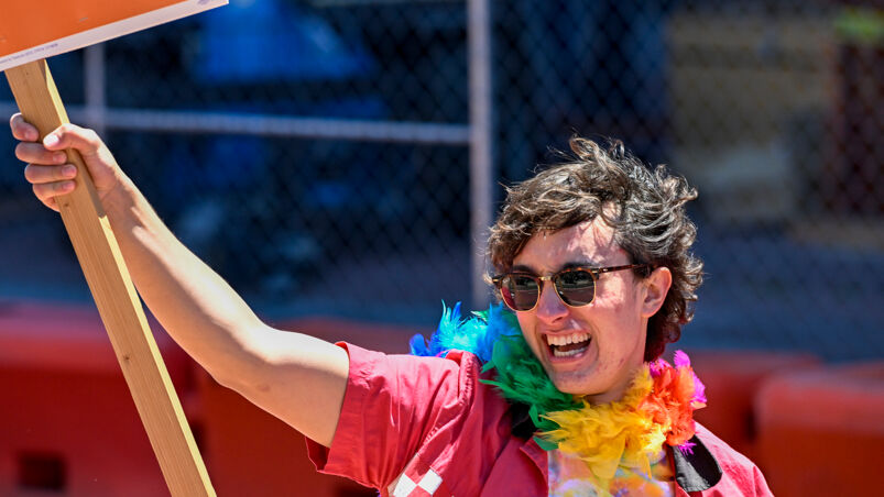 A young adult in a rainbow lei holds up a Trevor Project sign.