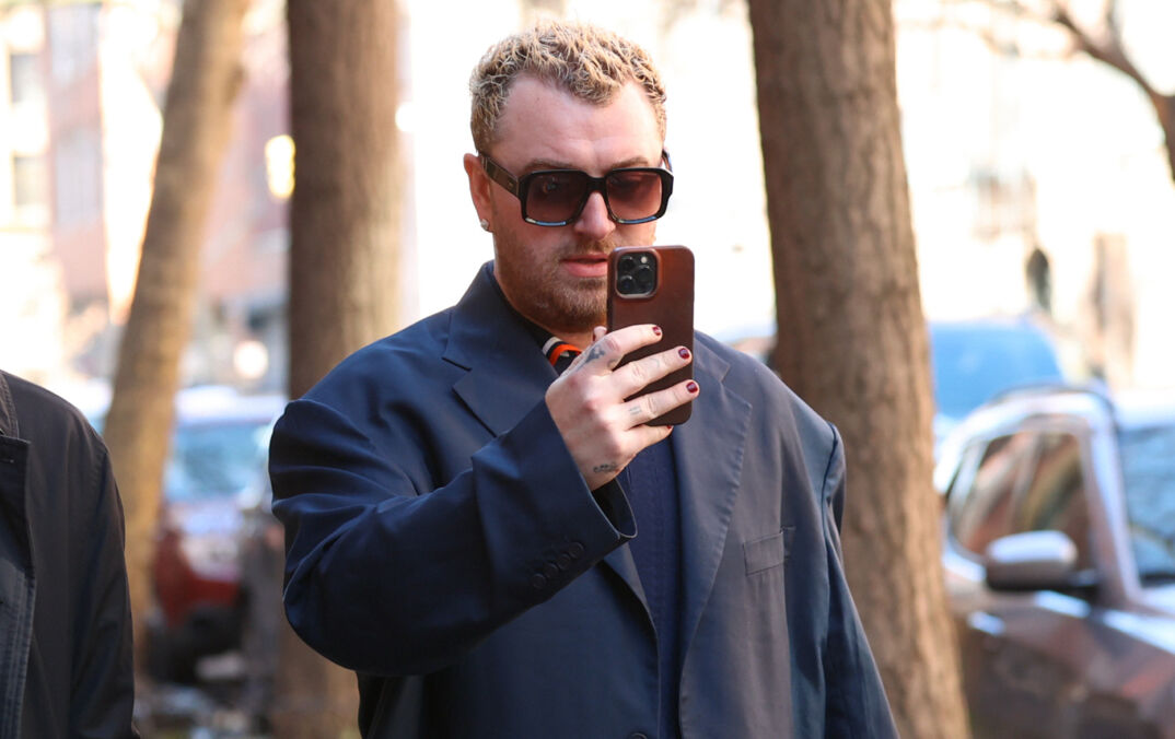 Sam Smith walking in New York City in a coat and shades.