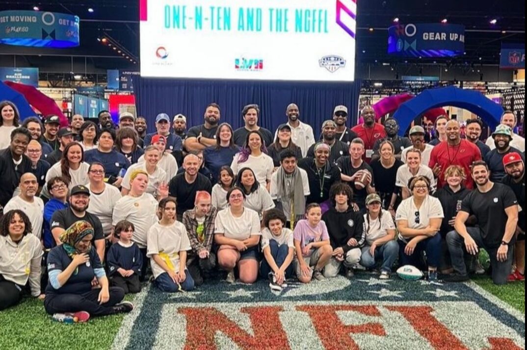 A large crowd poses for a picture behind the NFL logo painted on a football field.