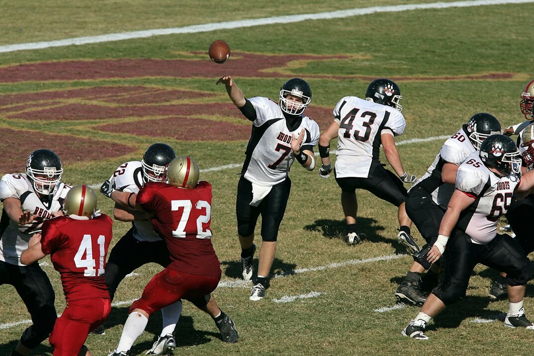 A quarterback throwing a football with his offensive line holding off the defense 