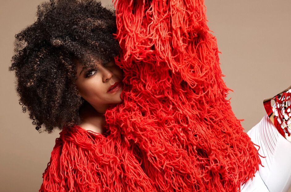 Crystal waters sprawled on her side, sporting an afro and a large fringe-laden red coat.