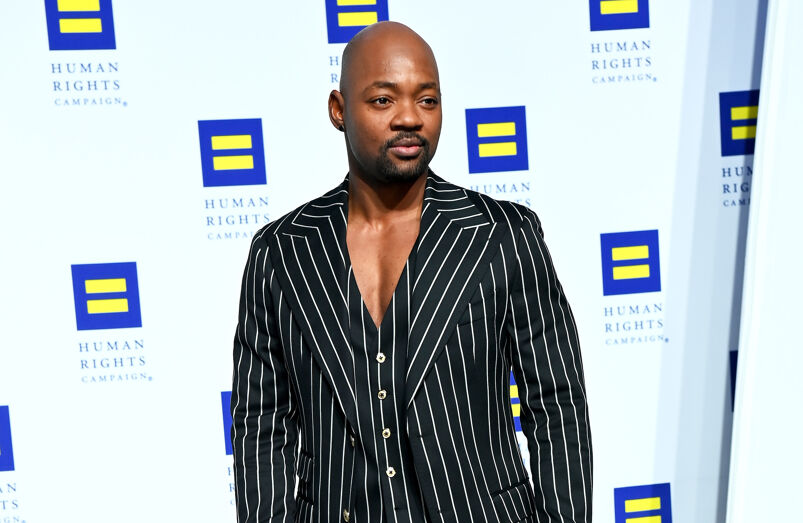 Actor Brian Michael Smith poses on the red carpet for the HRC Gala, wearing a black-and-white pinstripe suit with no undershirt.