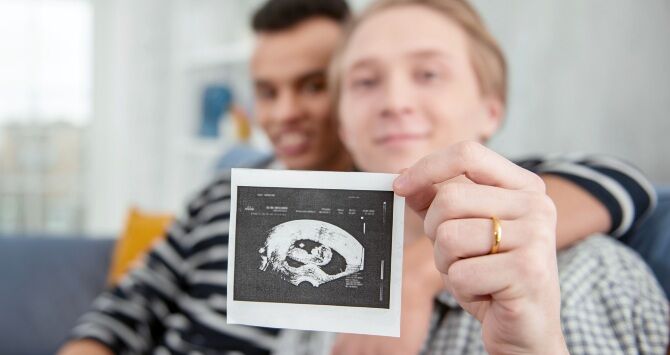 Two gay men hold up a sonogram image of a baby