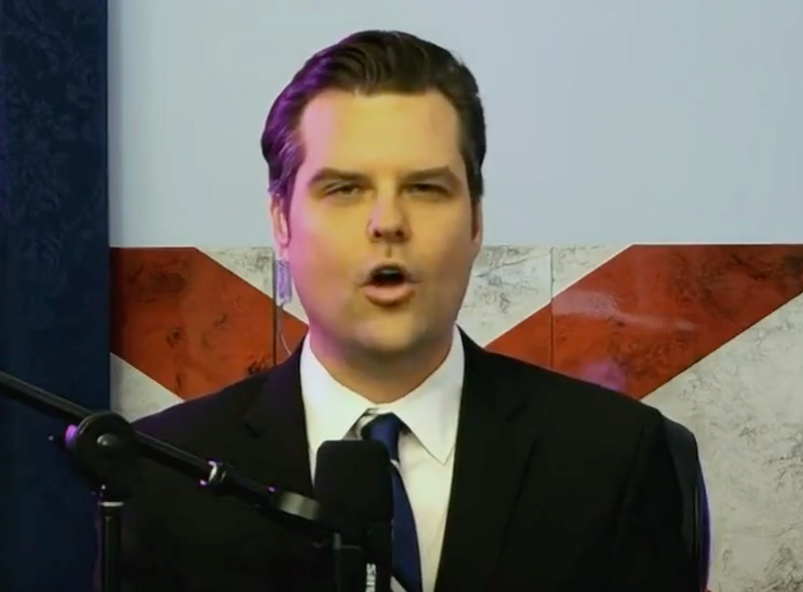 Matt Gaetz in a black suit and blue tie speaking into a microphone