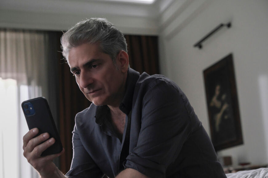 A still from 'The White Lotus: Sicily,' in which Michael Imperioli's character sits on a bed and looks at his phone.