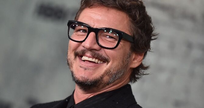 Pedro Pascal smiling with black glasses and a black shirt