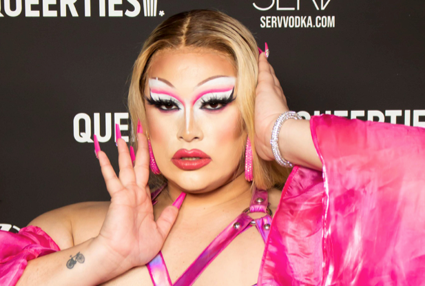 Salina Estitties poses in a blonde wig with a pic dress, top, and matching nails, against a black backdrop for the 2023 Queerties.