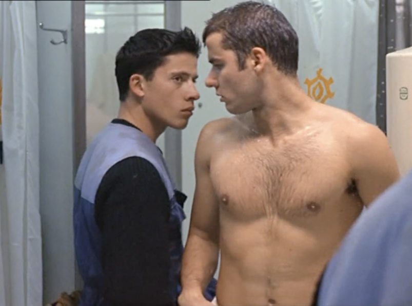 In a gym shower, one shirtless man and another in a trash-collector uniform stare intensely into on another's eyes.