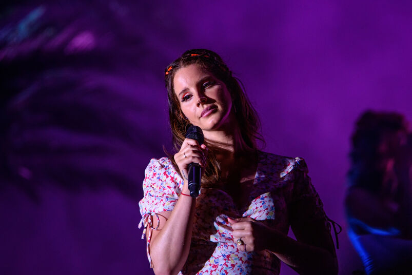 Lana Del Rey in a floral dress holding a microphone under a purple light