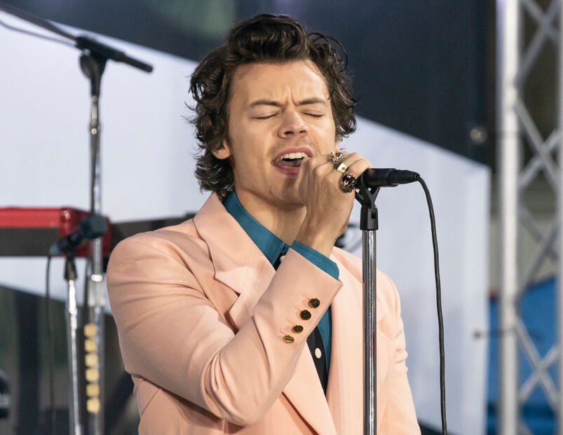Harry Styles in a peach jacket and blue shirt singing into a microphone