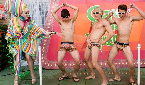 Three shirtless men in speedos get hosed down by drag queen Lady Bunny