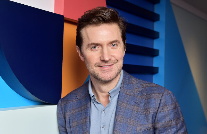 Wearing a blue blazer, actor Richard Armitage poses in front of a colorful wall
