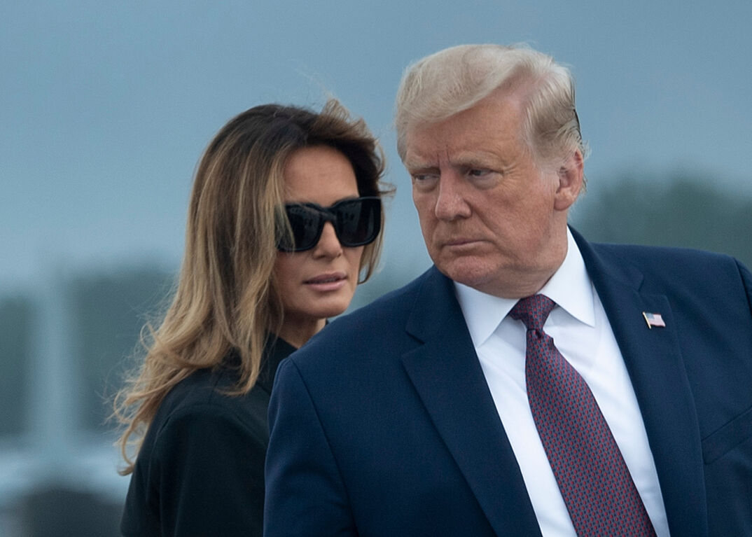 Melania Trump in sunglasses peering over Donald Trump's shoulder