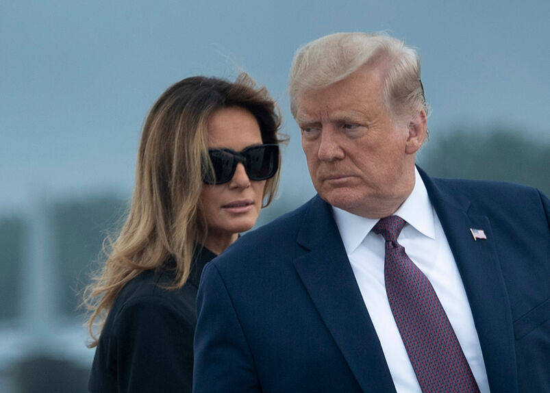 Melania Trump in sunglasses peering over Donald Trump's shoulder