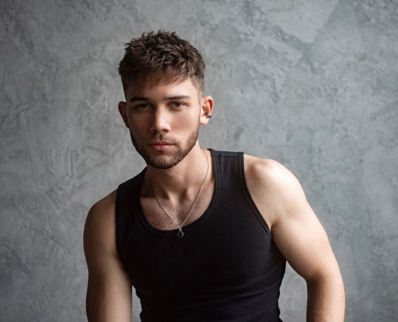 Singer Grant Knoche wears a black tank top in front of a grey wall.