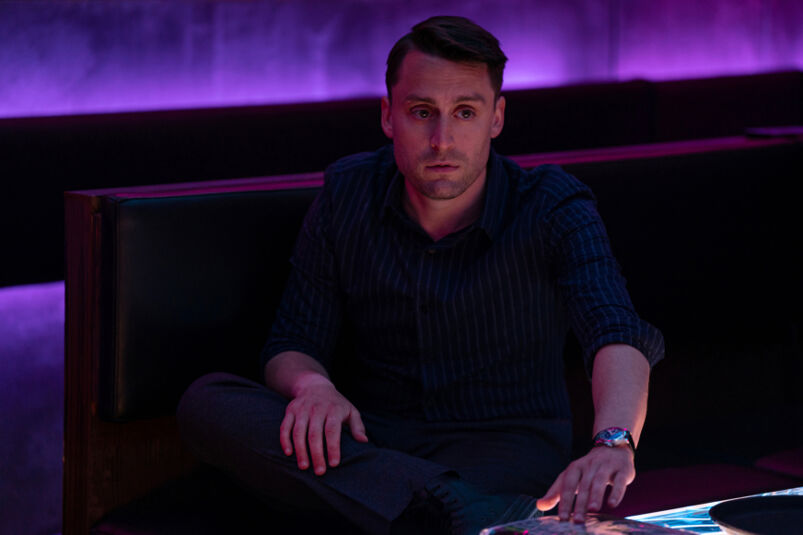 In Succession, Kieran Culkin wears a black shirt while surrounded by purple light