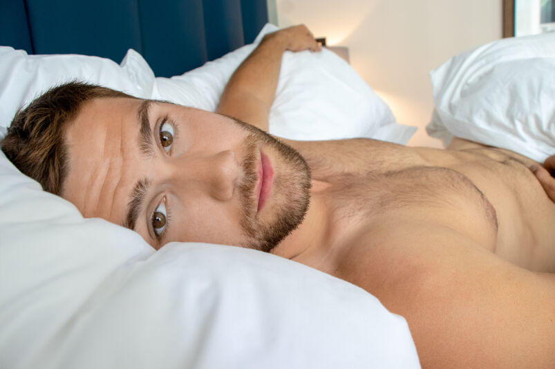 A selfie of a shirtless young man in bed. 