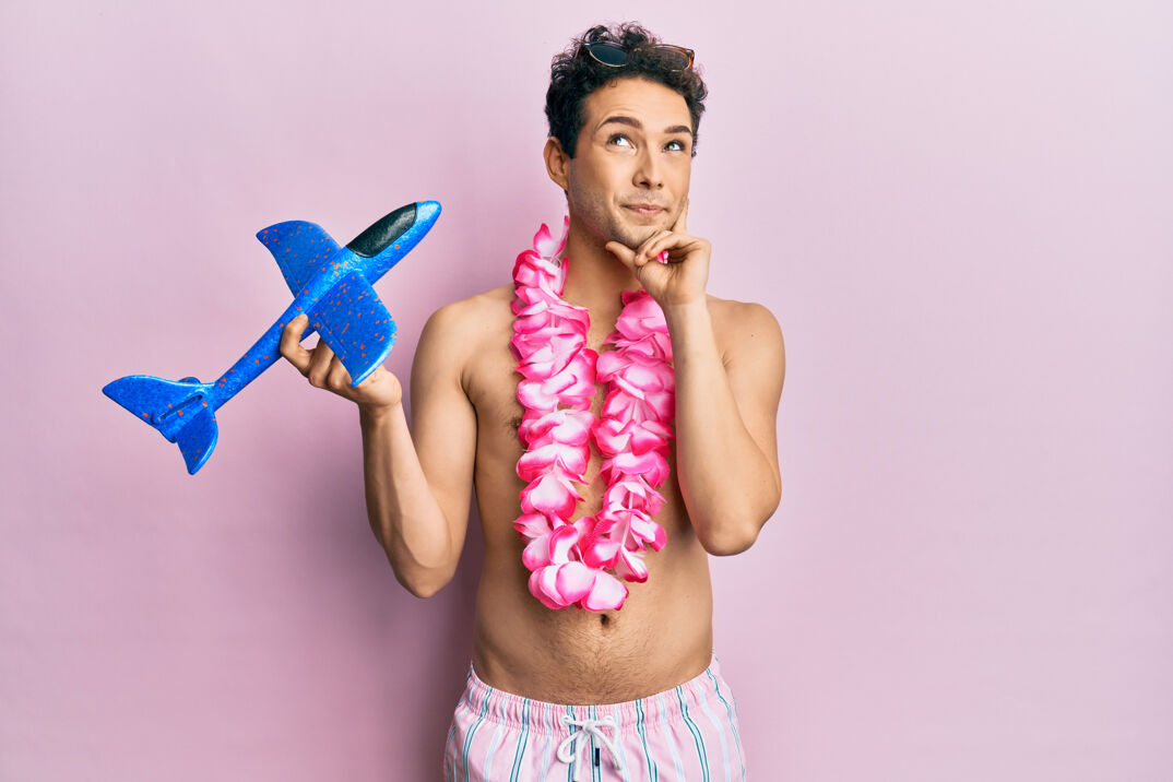 A man in a swimsuit wearing a lei and holding a toy airplane while thinking to himself