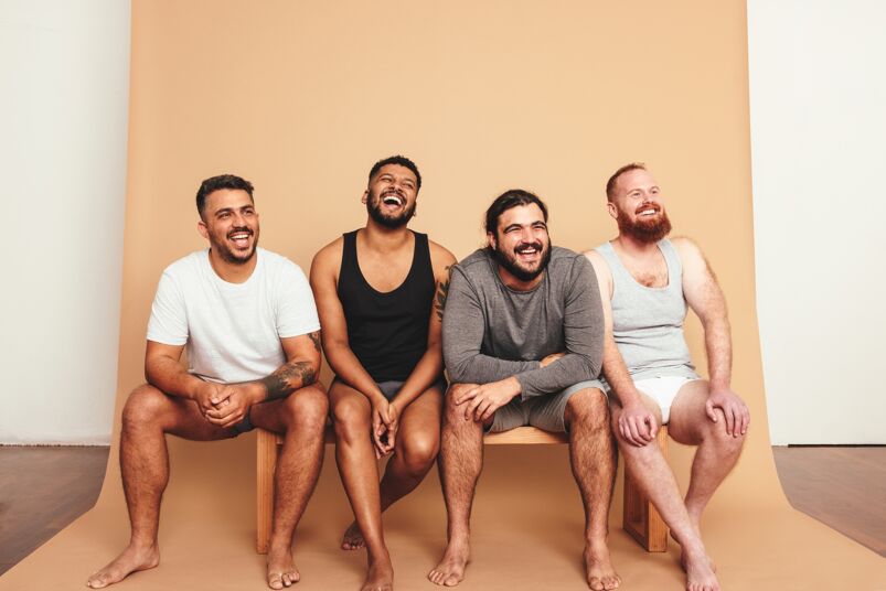 A group of four men sitting down and laughing with a tan backdrop.