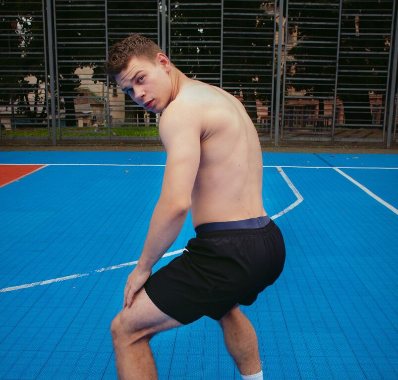Shirtless man squatting on a basketball court