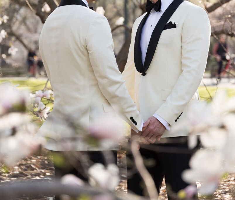 Two grooms holding hands wearing matching white tuxedos