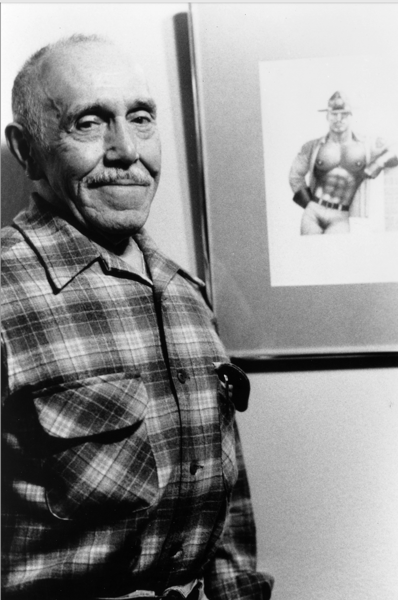 Tom of Finland smirking, standing in front of one of his drawings. 