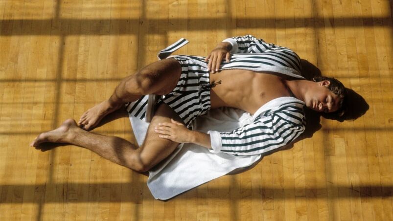 A man lays on the ground, his chest exposed, while wearing a black-and-white striped robe and matching shorts.