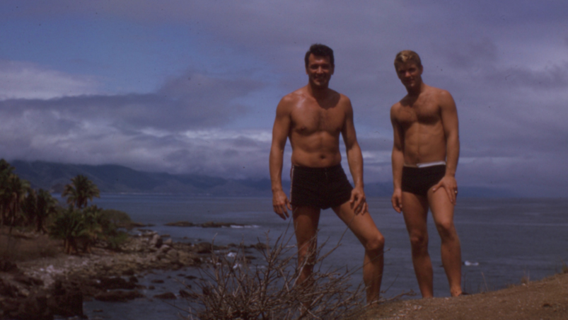 Actor Rock Hudson and a friend stand on a cliff in bathing suits.