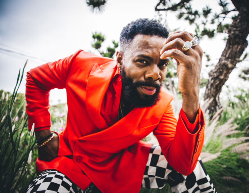 Colman Domingo poses outside in an orange double-breasted blazer and black-and-white checkered pants
