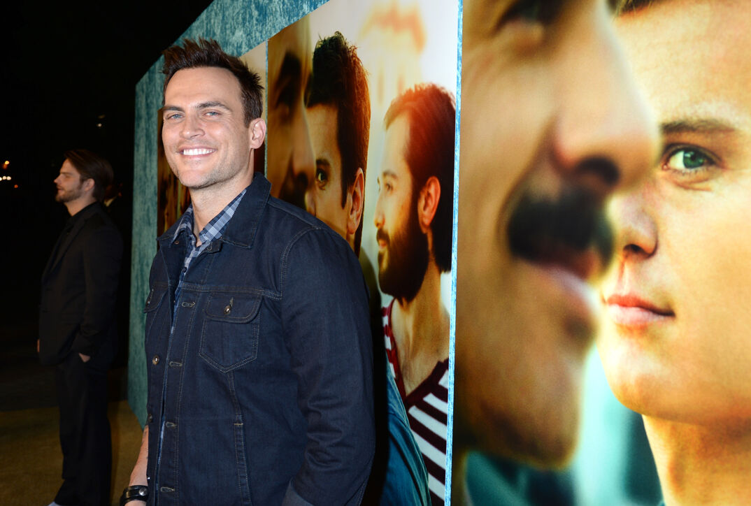 Cheyenne Jackson smiles on the red carpet in front of a poster for 'Looking.'