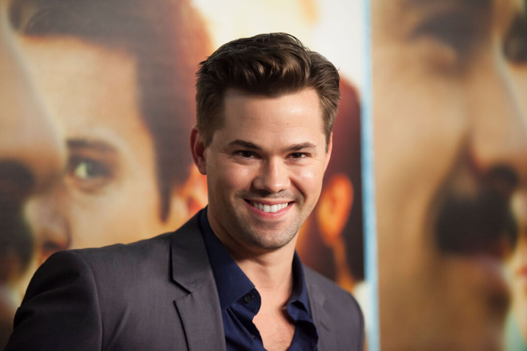 Andrew Rannells in a suit smiling on the red carpet.