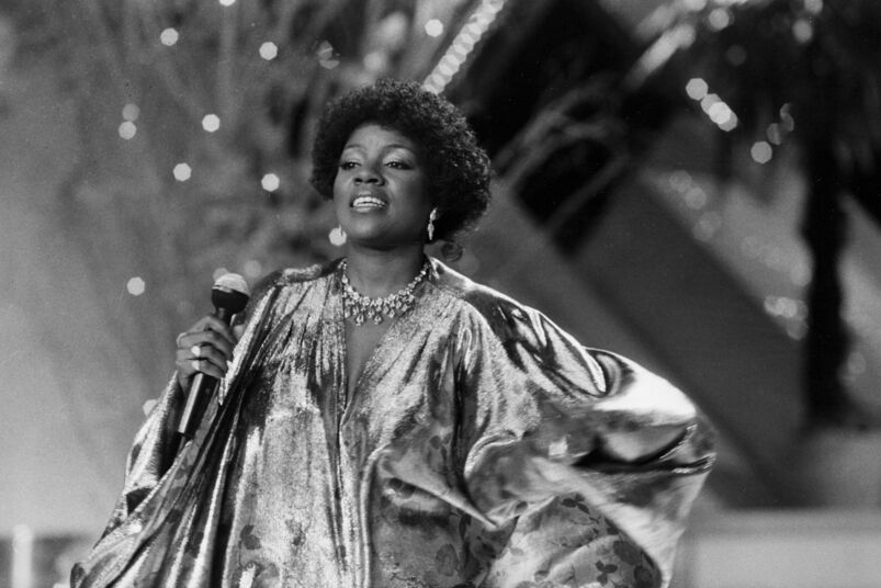 A black and white photo of Gloria Gaynor performing on a stage in front of lights in 1983.