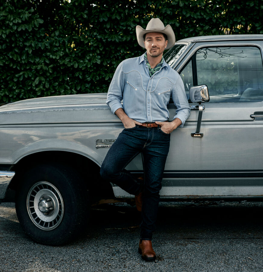 Jake Foy poses in a cowboy hat while leaning on a truck