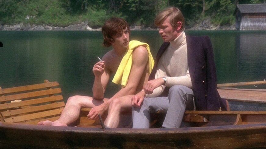 Michael York and a shirtless man sit on a boat in a still from 'Something For Everyone'
