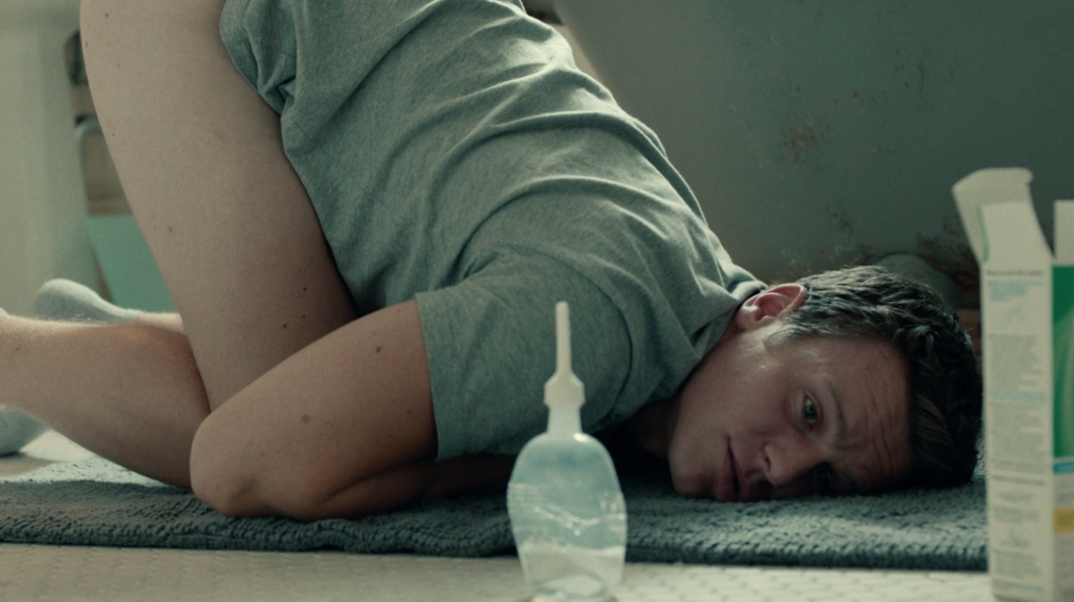 Jonathan Groff laying on a bathroom rug with his butt in the air and a fleet enema next to him.