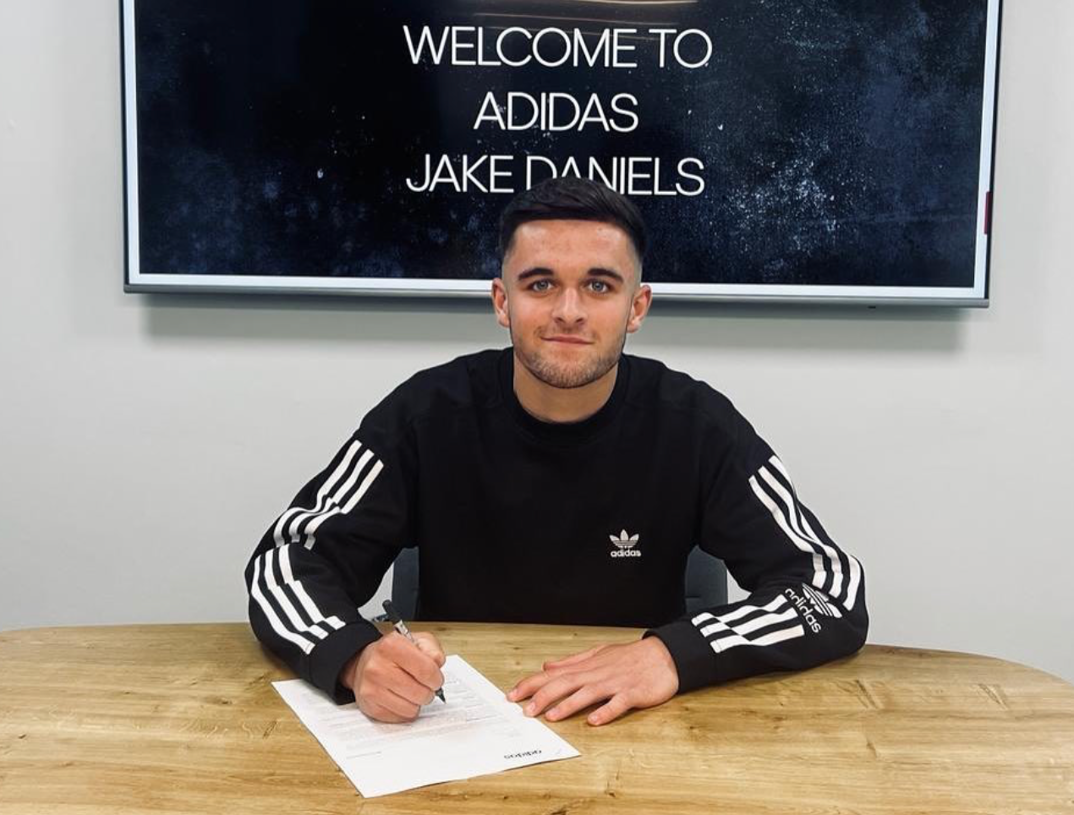 Jake Daniels wearing an Adidas shirt and signing an Adidas contract.