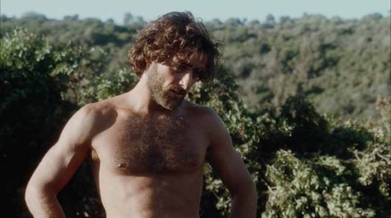 Adriano Giannini stands bearing his hairy chest in front of a forest of trees in a scene from 'Swept Away.'