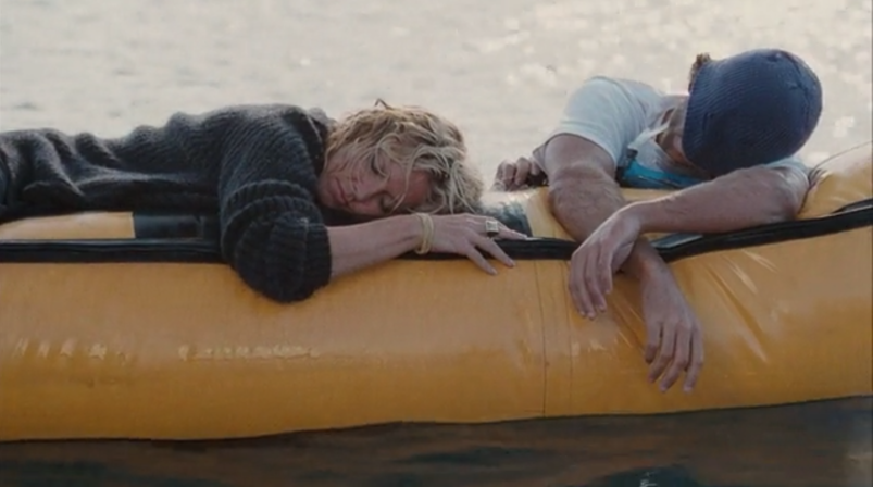 Madonna, wearing a black sweater and bracelet, lays against the side of a dinghy in the middle of the ocean. She is sleeping next to Adriano Giannini, who has a beanie over his face, in a scene from 'Swept Away.'