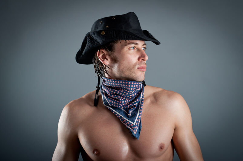 Shirtless man with cowboy hat and bandana on neck looking to the side. 