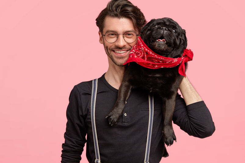 Man smiling wearing glasses with a black dog wearing red bandana resting on his shoulder. 