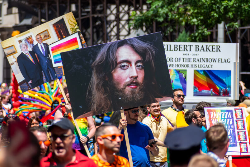 A crowd marching with signs of original Pride Flag creator Gilbert Baker. 